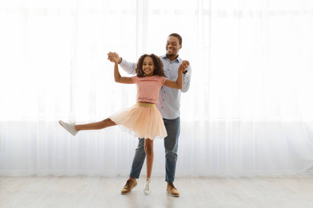 istock Black father and daughter dancing by window, full length shot 1325282391