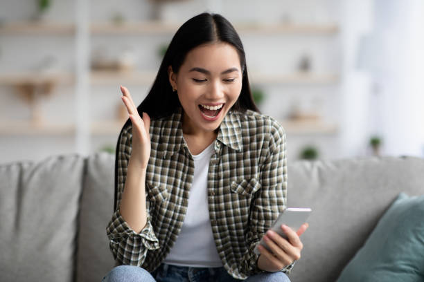 istock Emotional asian woman using smartphone at home 1325283010