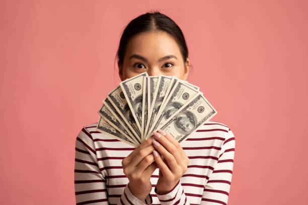 Big Profit. Happy Young Asian Woman Covering Face With Dollar Cash Fan Big Profit. Happy Young Asian Woman Covering Face With Dollar Cash Fan, Lucky Millennial Korean Female Holding Lots Of Money, Gor Prize, Standing Isolated Over Pink Background, Closeup Shot hand fan photos stock pictures, royalty-free photos & images