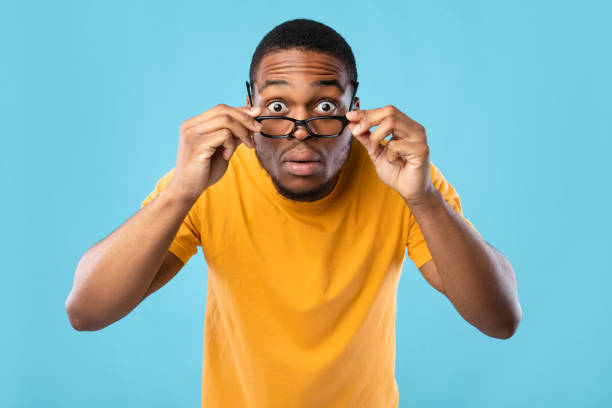 istock Shocked African Guy Looking At Camera Through Eyeglasses, Blue Background 1325283115