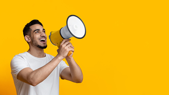 Tipo árabe emocionado hablando fuerte, usando megáfono en amarillo photo