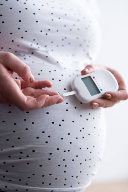 A pregnant woman holds a blood sugar meter in her hand and brings a test strip to a drop of blood on her finger stock photo
