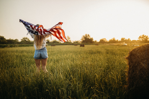 Woman holding USA on an agricultural field during sunset