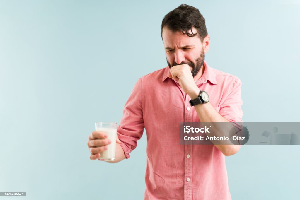 Latin man feeling unwell with nausea Upset man trying to drink a glass of milk and feeling nauseous. Lactose intolerant guy covering her mouth and eating dairy products Lactose Fermentation Stock Photo