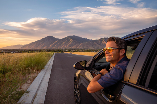 A man enjoys the view while parked in his new car. Utah sunset.