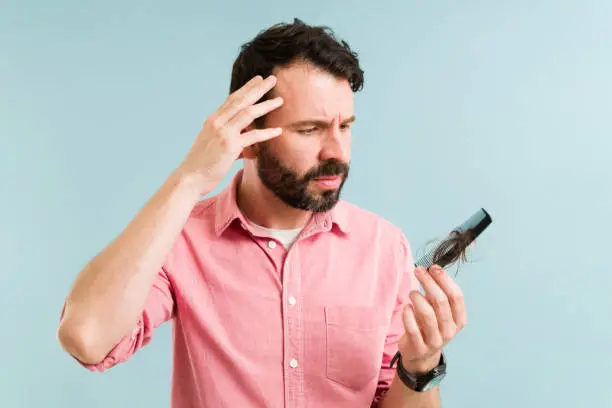 Hispanic man combing his hair while feeling worried and sad because of his hair loss. Stressed man starting to go bald