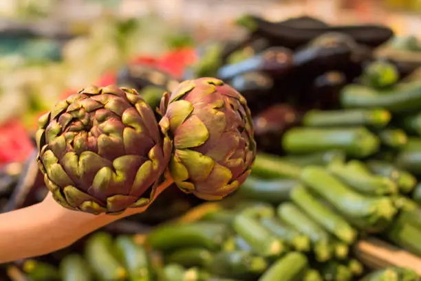 Photo of Female hand choosing artichoke in the store. Concept of healthy food, bio, vegetarian, diet.