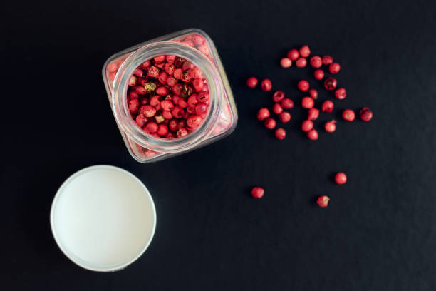 rosa pfefferkörner in einem glas auf dunklem hintergrund, flache schärfetiefe, blick oben - pink pepper stock-fotos und bilder