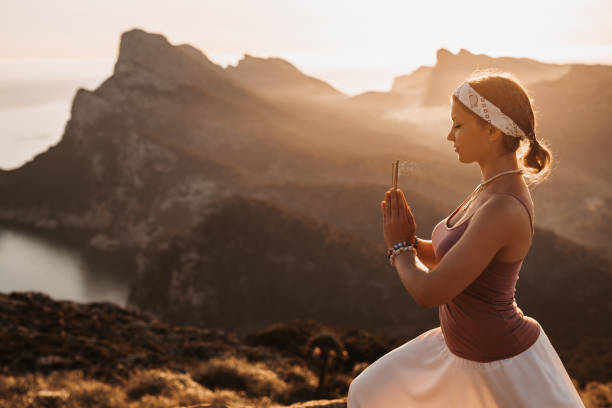 istock Meditative woman with closed eyes doing meditation standing with incense sticks during the sunrise in a mountainous landscape 1325296510