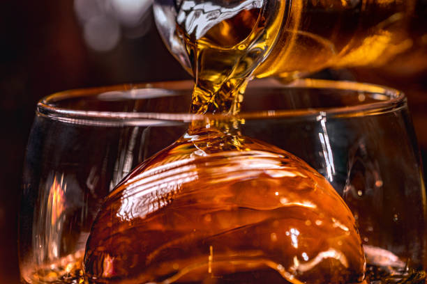 Liquid pouring Ice Tea or liquor being poured over an ball ice in a glass macro pouring stock pictures, royalty-free photos & images