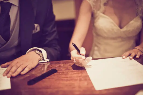 Couple signing their wedding day in detail shot with selective focus and vintage tone.