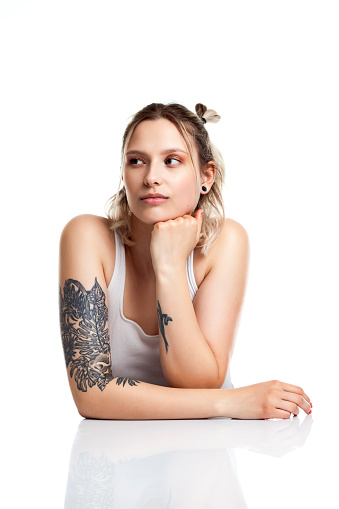 Portait of a young woman with tattoos sitting at a white reflective table