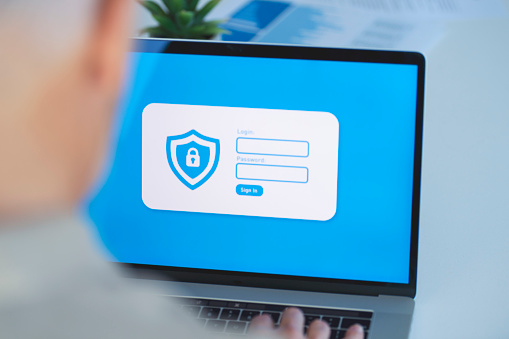 Businessman logging on to a password protected website. There are login and password fields and a sign in button. There is also a shield and lock graphic