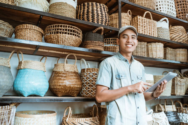 smiling young entrepreneur while holding a digital tablet with a hand-crafted bag in the background smiling young entrepreneur looking at the camera while holding a digital tablet while standing with a hand-crafted bag in the background malay stock pictures, royalty-free photos & images