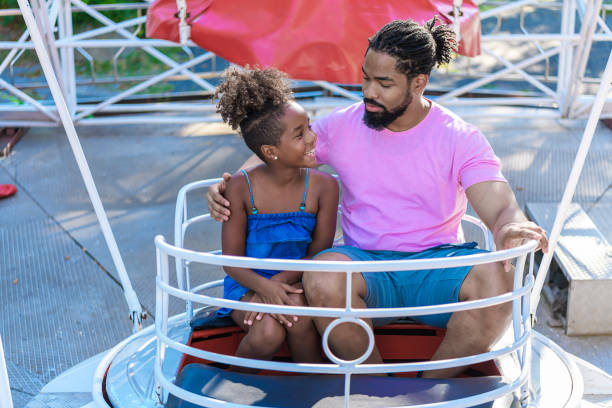 padre e hija están pasando un tiempo maravilloso en carrusel en el parque de atracciones. - carousel merry go round child african descent fotografías e imágenes de stock