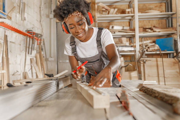 una trabajadora africana está usando una cinta métrica y un lápiz para marcar la tabla de madera antes de cortar. - craft project fotografías e imágenes de stock