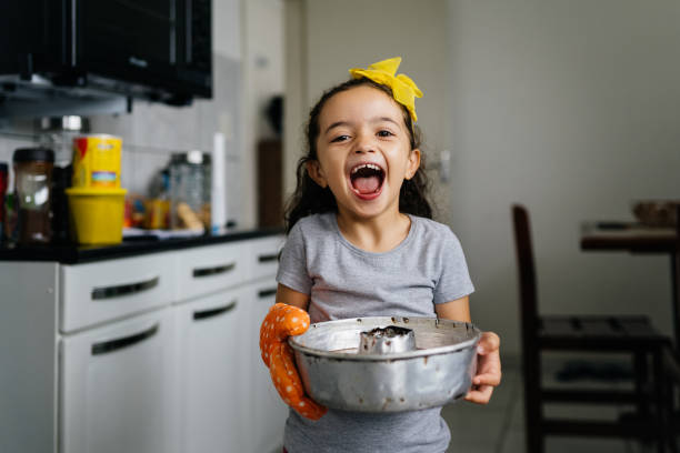 happy little girl holding a cake tin in the kitchen - little cakes imagens e fotografias de stock
