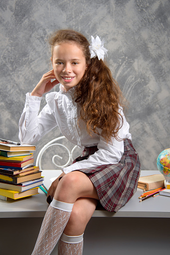The fidget schoolgirl in school uniform sits on table and smiles happily on a light gray background. Back to school. The new school year. Child education concept.