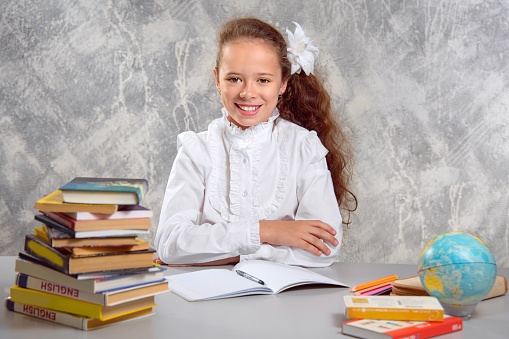 The schoolgirl in school uniform sits at the desk and and smiling at the viewer. Back to school. The new school year. Child education concept.