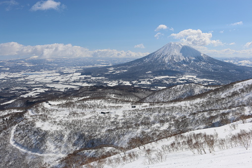 Snow-covered mountains of Niseko ski resort with Mt Yotei in the distance on a sunny day