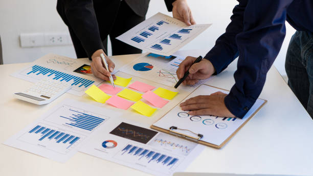 istock Businesswomen and men reading financial reports, discussing, analyzing, calculating graph documents that Asian female and male managers discuss and scrutinizing negotiation decisions. work as a team at work 1325334096