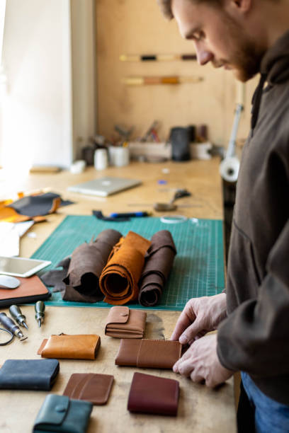 istock Craftsman hands laying out leatherwork on wooden table at leather workshop. Handwork accessories 1325336919