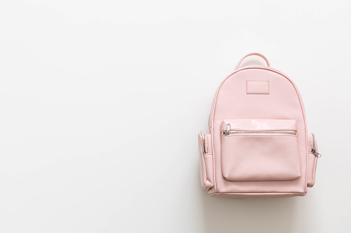 Elegant leather pink female backpack isolated on white background with copy space top view. Stylish bag with zipper and pocket for carrying college or university supplies. Back to school concept