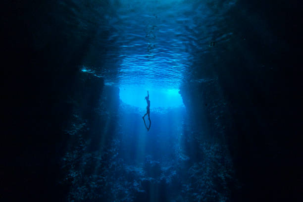 Diver swimming in underwater cave towards the light at ocean's surface Ocean Diver swimming through the deep blue in an underwater cave towards the sunlight at water’s surface underwater diving stock pictures, royalty-free photos & images