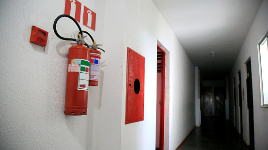 Dry chemical powder fire extinguisher in corridor. Install a fire extinguisher on the wall in building. A red fire-extinguisher hangs on wall .