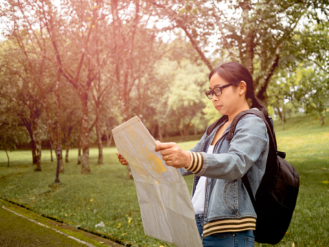A female tourists with backpack relaxing outdoor and searching right direction on map in the forest. Freedom and lifestyle on vacation concepts.