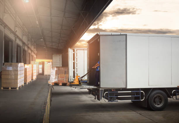 package boxes on pallets loading into cargo container. trucks parked loading at dock warehouse. delivery service. shipping warehouse logistics. road freight truck transportation. - vervoer stockfoto's en -beelden