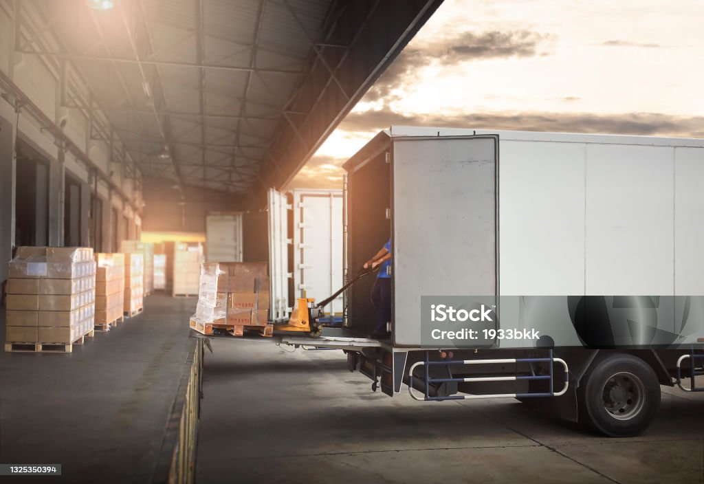 Package Boxes on Pallets Loading into Cargo Container. Trucks Parked Loading at Dock Warehouse. Delivery Service. Shipping Warehouse Logistics. Road Freight Truck Transportation. Truck Stock Photo