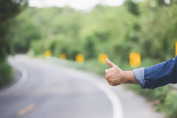 Photo of Pick me up. Man hitchhiking on the side of the road. Man try stop car thumb up. Hitchhiking one of cheapest ways traveling.
