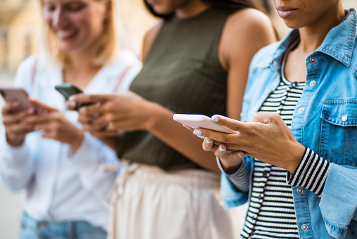 Three woman on the street using mobile phone.  Focus is on hands.