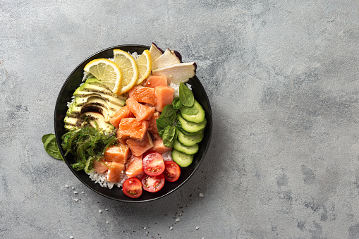 Poke bowl with salmon, avocado and vegetables on light background overhead view