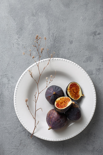 Sliced and whole fresh figs in bowl on light background top view