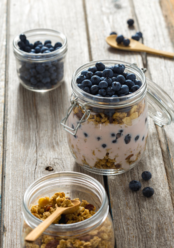 Organic granola breakfast with yogurt and blueberries in glass jar on wooden table