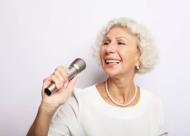 istock Happy senior woman singing with microphone, having fun, expressing musical talent 1325355467