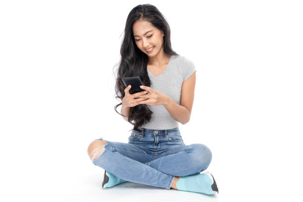 ritratto di una donna asiatica si siede sul pavimento usando uno smartphone. isolato su sfondo bianco - floor sitting foto e immagini stock