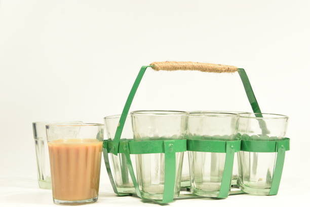 Chai (Indian tea) cups/glasses along with a glass stand to carry the glasses A filled glass of tea with a few empty ones along with a green colour metallic tea glass holder/stand, used for serving chai (Indian tea), with a white background. sabby stock pictures, royalty-free photos & images