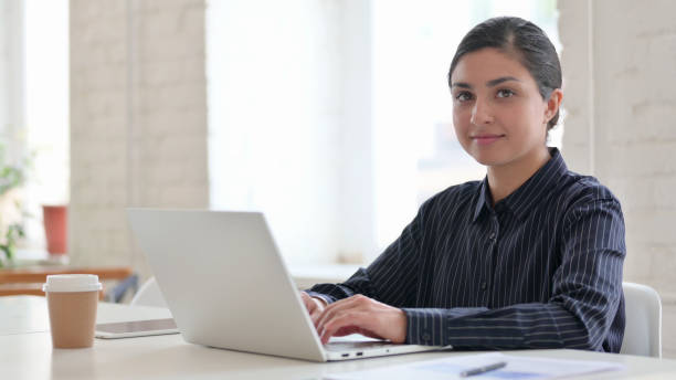 istock Young Indian Woman with Laptop Looking at Camera 1325362861