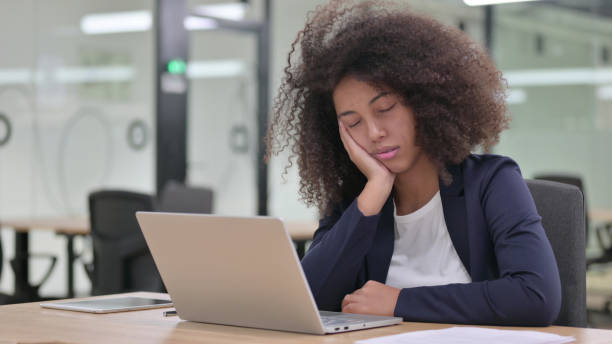 сонная молодая африканская бизнесвумен с ноутбуком, имеющих nap - yawning стоковые фото и изображения