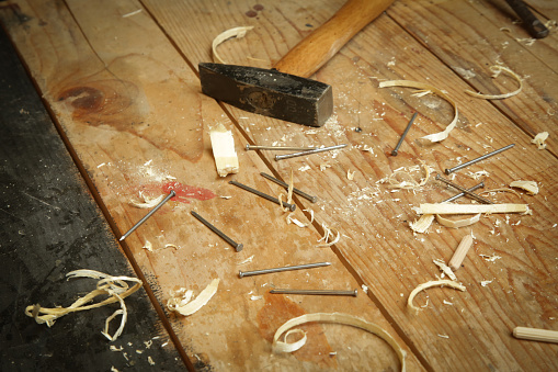 Workshop with tools on the wooden table. Hammer and wooden shavings close up.