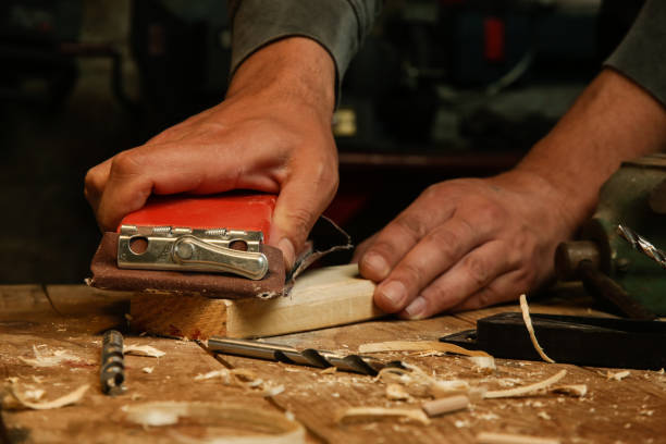 istock Carpenter is using sandpaper on a piece of wood in workshop. Sanding wooden plank. 1325366397