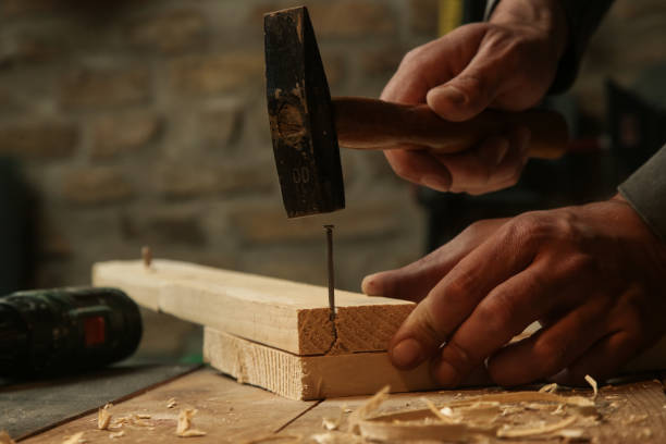 istock Carpenter hammering nail into wooden plank in workshop. 1325366618