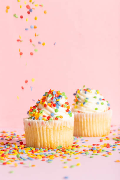 White cream cupcake with color sprinkles on rose White cream cupcake with color sprinkles on rose. High quality photo white wedding cake red roses stock pictures, royalty-free photos & images