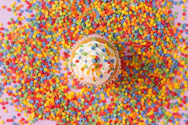 White cream cupcake with color sprinkles on rose White cream cupcake with color sprinkles on rose. High quality photo white wedding cake red roses stock pictures, royalty-free photos & images