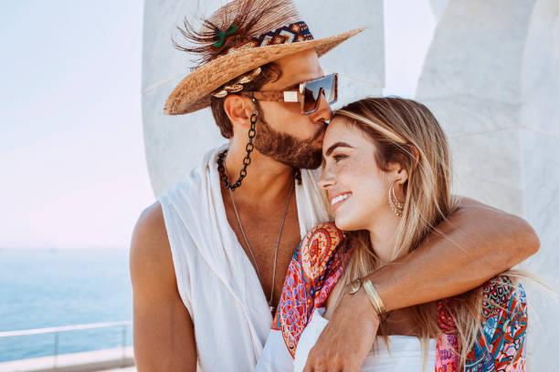 Man kissing blonde woman on forehead Close up of attractive young couple embracing on beach. Bearded man kissing blonde woman on forehead. Sea background on beautiful morning light at summer straw hat photos stock pictures, royalty-free photos & images