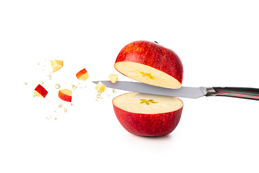 Front view of a red apple being cut in halves by a kitchen knife with some apple juice drops and some bites on the air.