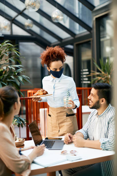 istock Waitress wearing protective face mask while serving couple in a cafe, 1325380258